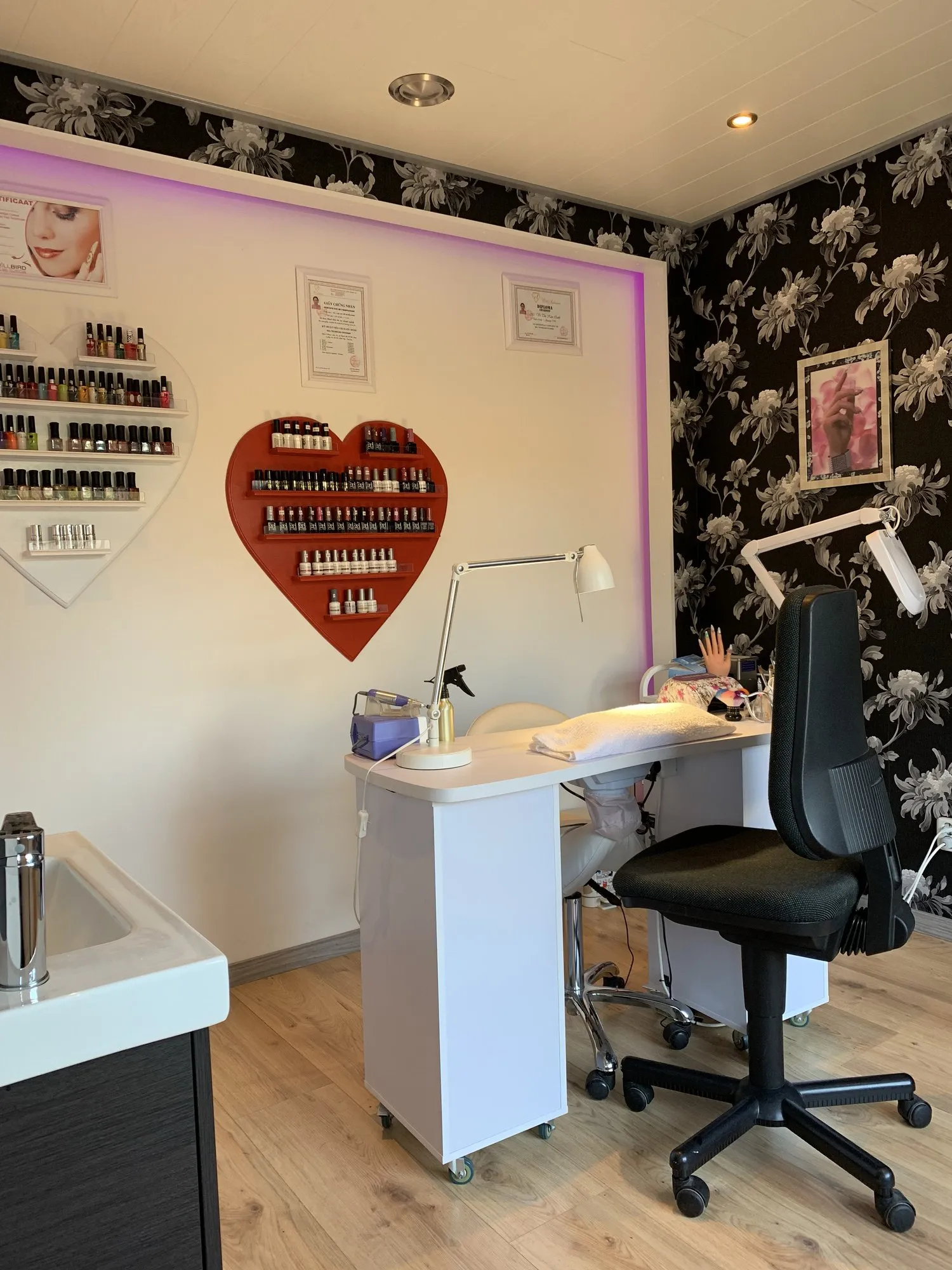 De nagelstudio van Kim met werktafel, roze verlichting en een hartvormig rek vol nagellak